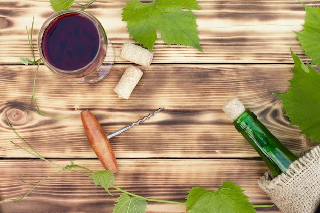 Wine glass, corkscrew, corks, wine bottles, grapevine on rustic burnt wooden background. Top view. Copy space