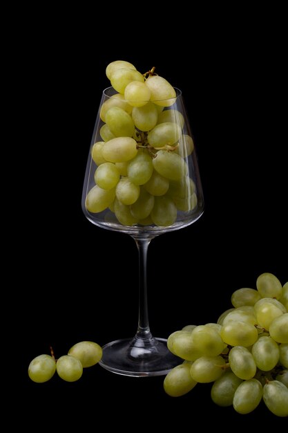A wine glass filled with green grapes on a black background.