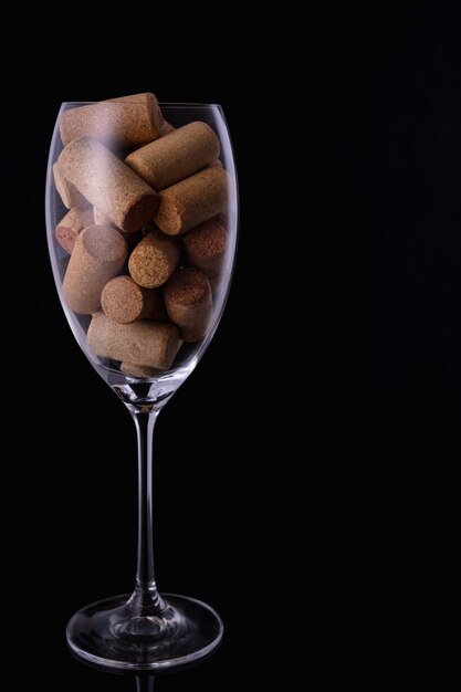 Wine glass full of wine corks on black background