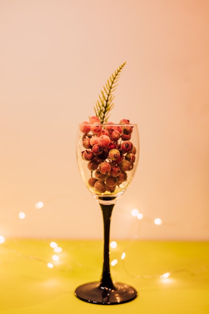 Wine glass on a long stem filled with decorative berries with a sprig of spruce