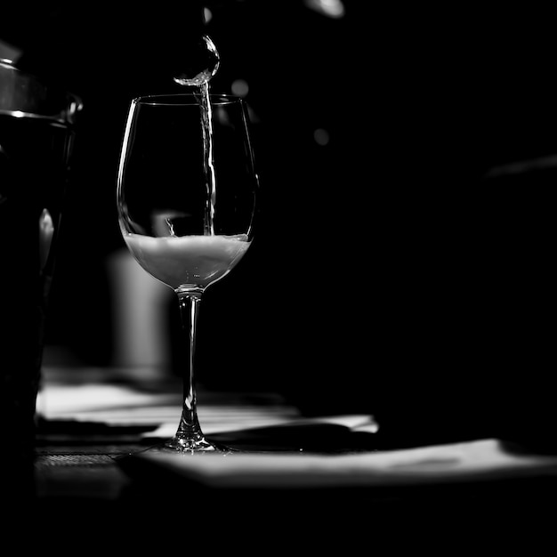 The wine glass stands on the table and a trickle of champagne is poured into it. BW.