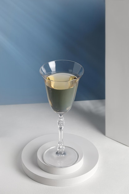 Wine in glass on white podiums. Glass of wine on pedestal in sunlight. Shadow on blue wall.