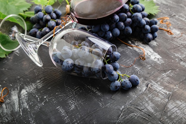 Wine glasses full of grapes on black stone table. Grape bunches with leaves and vines on dark rustic concrete background. Wine glass composition with grape imitated fresh red wine.