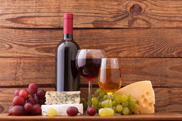 Wine glasses near cheese and ripe grape on wooden deck