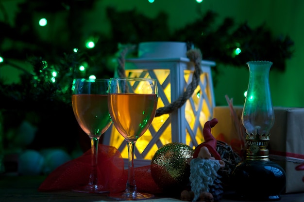 크리스마스 트리와 랜턴 근처의 와인 잔 - 새해 기쁨을 가져올 준비가 된 선물. 초록불