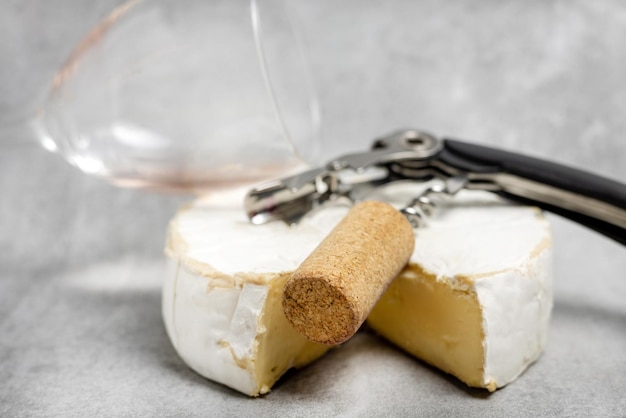 Photo wine opener accessories toolsrose bottle and brie camembert cheese isolated gray tiles backgroundg