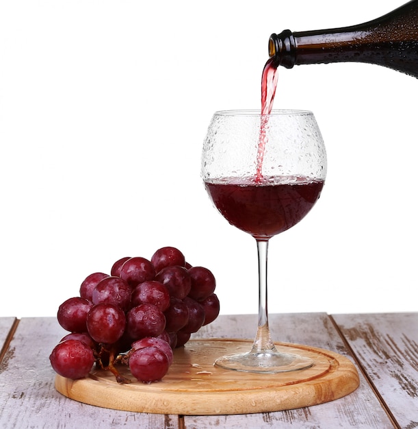 Wine pouring into glass with grape and bottles isolated