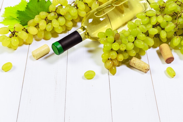 Wine with branches of white grapes. On a wooden table.