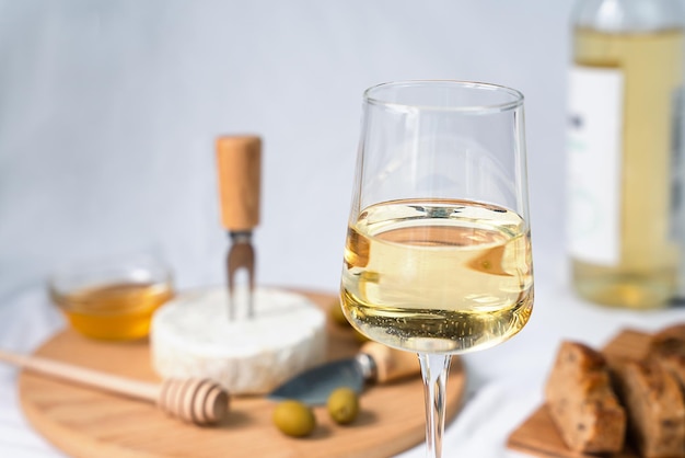 Foto un bicchiere di vino bianco e sullo sfondo il formaggio camembert baguette olive e miele sul tavolo closeup focus selettivo