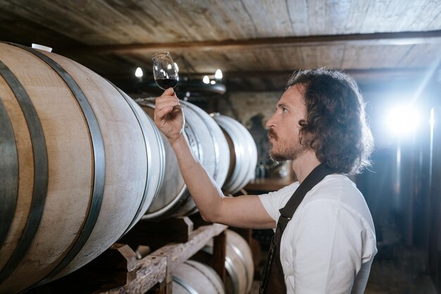 Foto enologo che degusta vino in una cantina con botti di legno