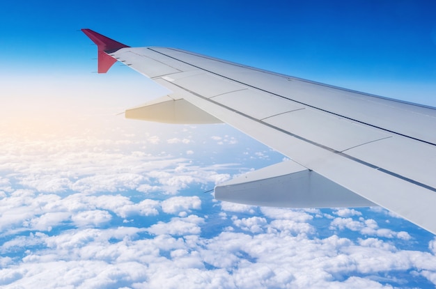 雲と飛行中の飛行機の翼。旅行と新しい国へのフライトの概念