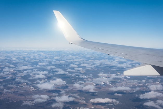 雲の上を飛んでいる飛行機の翼、旅行する航空輸送。バックライト太陽光線。