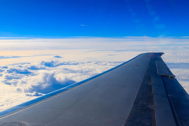 Wing of airplane flying above the clouds in the blue sky