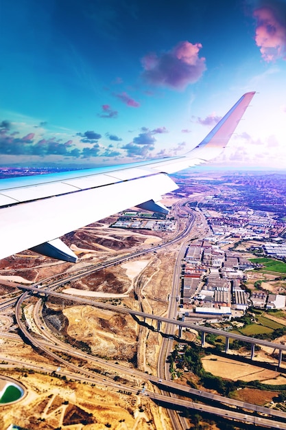 Wing of an airplane flying over industrial buildings warehouses and roads