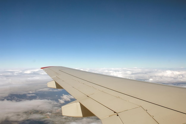 The wing of a passenger plane flying in the sky against a blue sky with clouds copy space