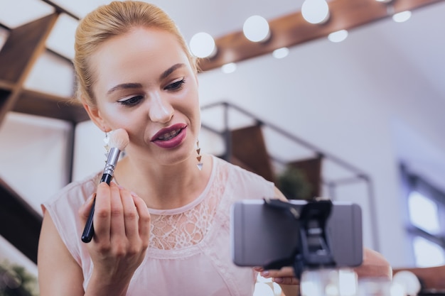 Winged eyeliner. Appealing blonde-haired woman with bright makeup and winged eyeliner filming beauty blog