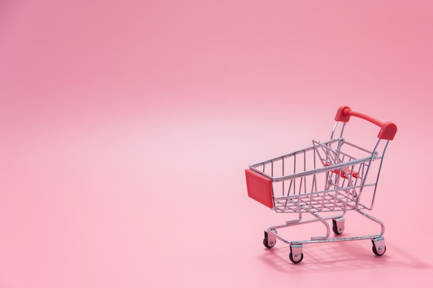Winkelconcept - lege rode winkelwagentje op roze achtergrond