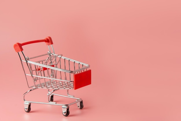 Winkelconcept - rode winkelwagentje op roze achtergrond met kopieerruimte