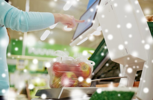 Foto winkelen consumentisme en mensen concept vrouwelijke klant het wegen van appels op de schaal bij de supermarkt over sneeuw