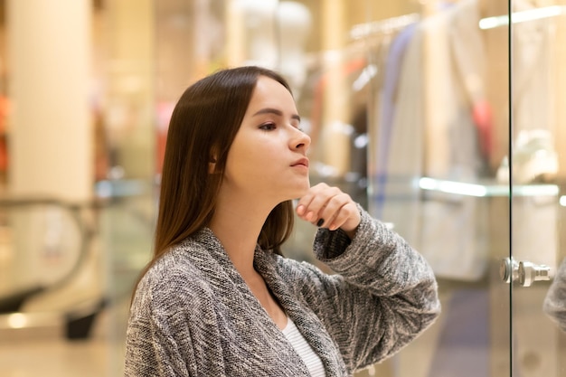 Winkelen Een jong meisje kijkt naar etalages, glimlacht, doet aankopen in een winkelcentrum.