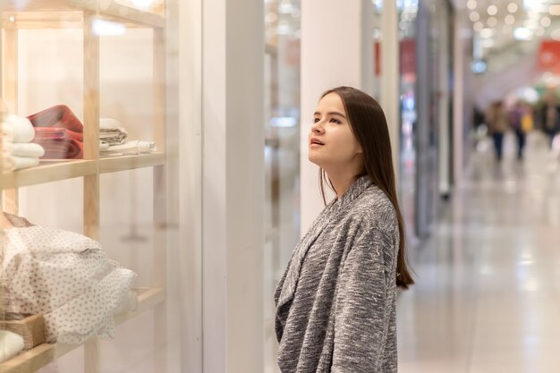 Winkelen Een jong meisje kijkt naar etalages, glimlacht, doet aankopen in een winkelcentrum.