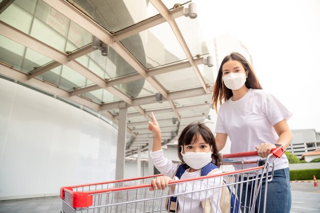 Winkelen met kinderen tijdens een virusuitbraak. Aziatische moeder en dochter die chirurgisch gezichtsmasker dragen die naar de supermarkt gaan.