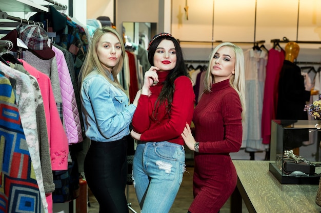 Winkelen, mode en vriendschapsconcept - drie lachende vrienden die wat kleren proberen in het winkelcentrum.