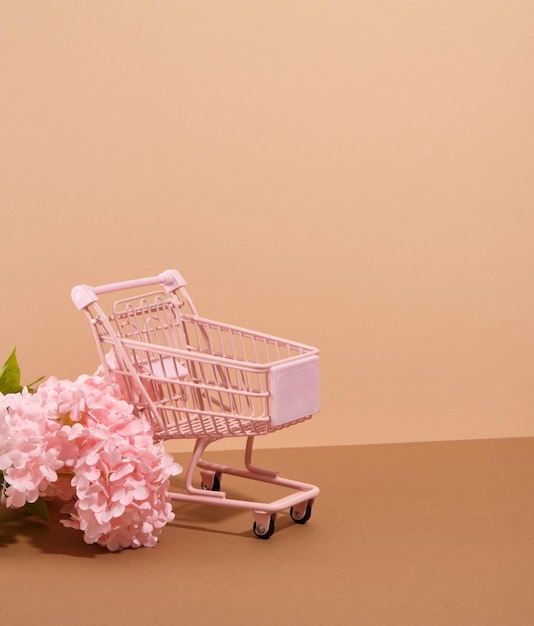 Winkelen online concept Roze leeg winkelwagentje en mooie zomerbloemen Kopieer ruimte voor tekst