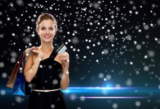winkelen, verkoop, bankieren, geld en vakantie concept - lachende vrouw in jurk met boodschappentassen en creditcard op zwarte achtergrond