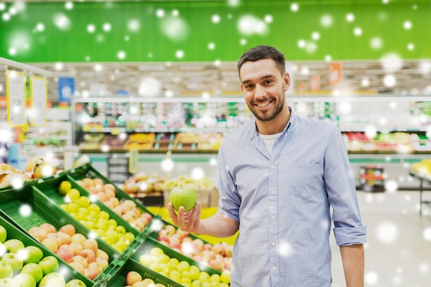winkelen, voedselverkoop, consumentisme en mensenconcept - gelukkige man die groene appels koopt in de supermarkt of supermarkt over sneeuw