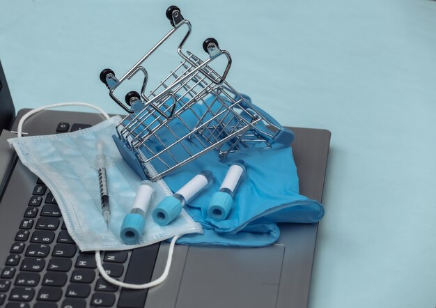 Winkelkarretje, medisch masker, reageerbuisjes, handschoenen met spuit op laptop toetsenbord. Covid-19-pandemie