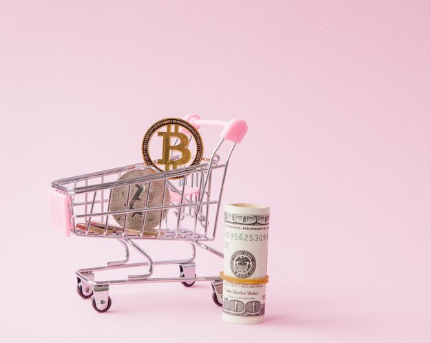 Winkelwagen met bitcoin munt en dollars op roze