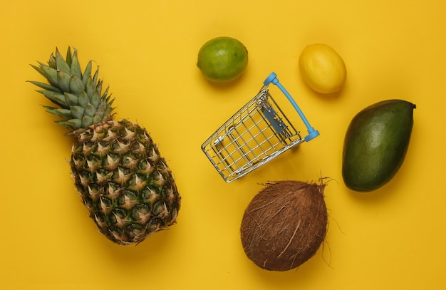 Winkelwagentje en tropisch fruit op een gele achtergrond. Winkelen in de supermarkt. Gezond voedselconcept