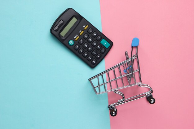 Winkelwagentje met rekenmachine op roze blauw. Economische berekening van boodschappen, aankoopkosten.