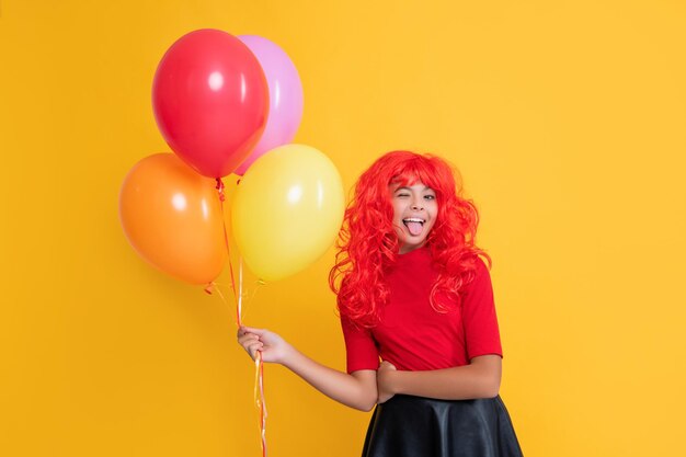 Winking child with helium balloon on yellow background