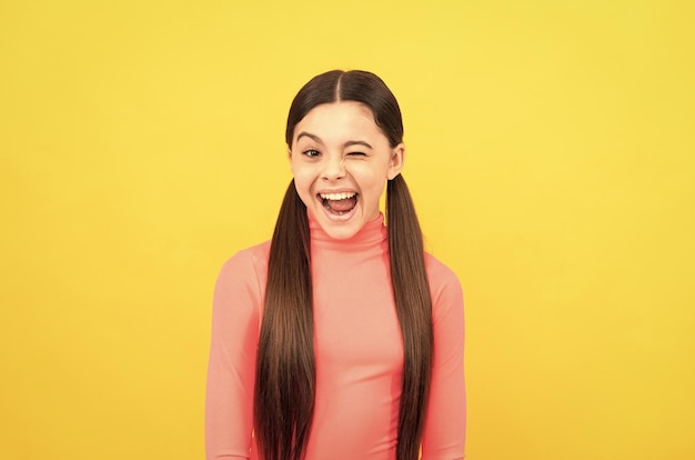 Winking child with long hair on yellow background emotions