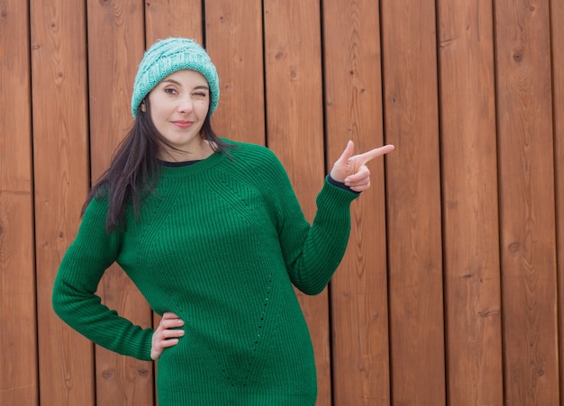 Winking european woman in green sweater and green hat on wooden wall