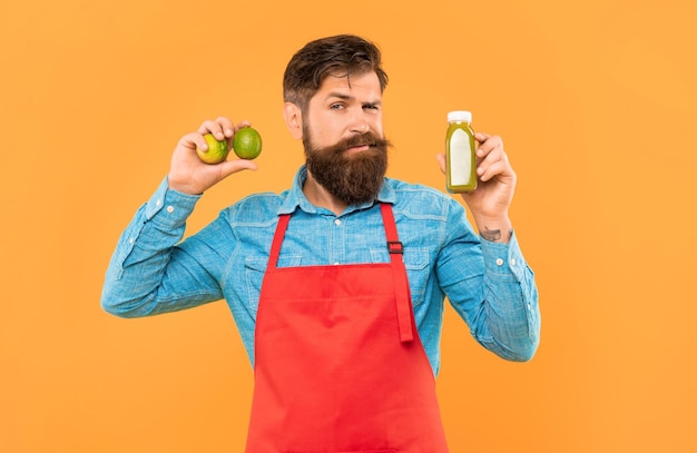winking man in apron holding limes and juice bottle yellow background juice barman