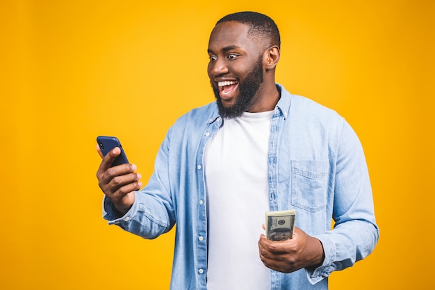 Winnaar! Jonge rijke Afro-Amerikaanse man in casual t-shirt met geld dollarbiljetten en mobiele telefoon met verrassing