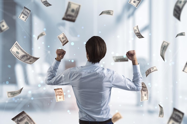 winner power business success and money concept with joyful man back view under dollar banknotes rain on blurred office background
