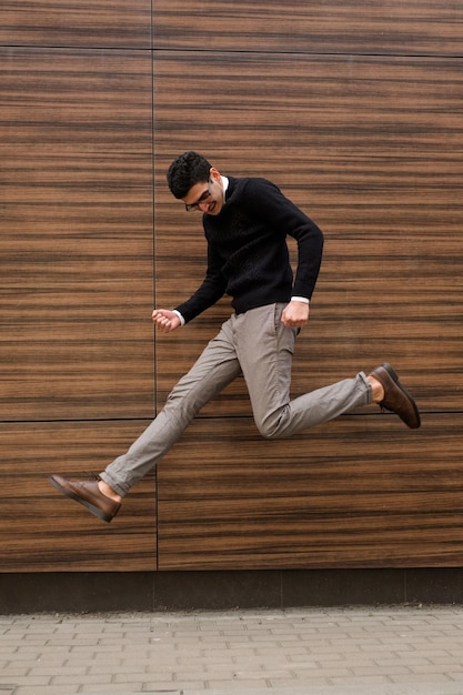 winner success happiness confidence. casual business man expressing emotions with like a rockstar mid air jump motion. wood texture wall background. outdoors street. copyspace concept