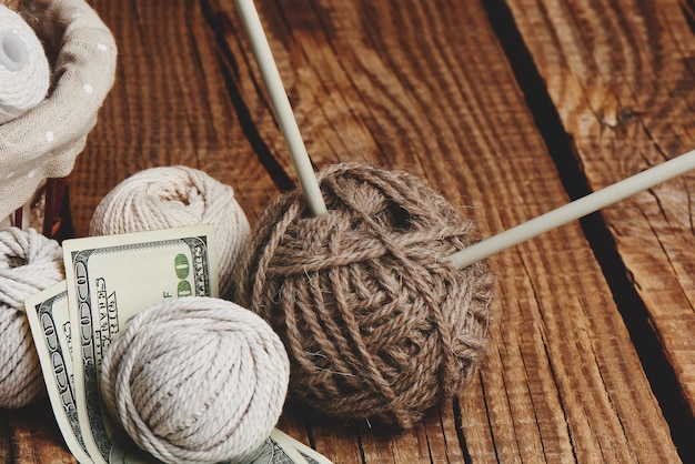 Winstgevende hobby. Verdiensten op handwerk. Ballen van natuurlijke kleur garen, breinaalden en geld op een houten tafel.