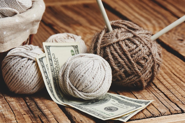 Winstgevende hobby. Verdiensten op handwerk. Ballen van natuurlijke kleur garen, breinaalden en geld op een houten tafel.