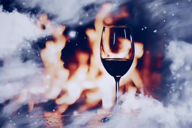 Winter atmosphere and Christmas holiday time glass of wine in front of fireplace covered with snowy effect on window glass holidays background