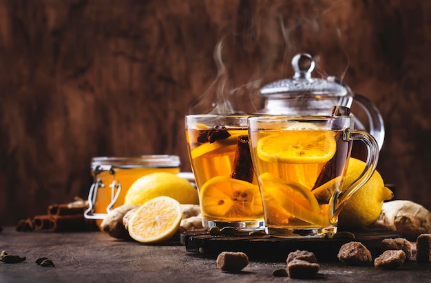 Winter or autumn hot healing tea with ginger honey lemon and spices in glass cup with steam rustic