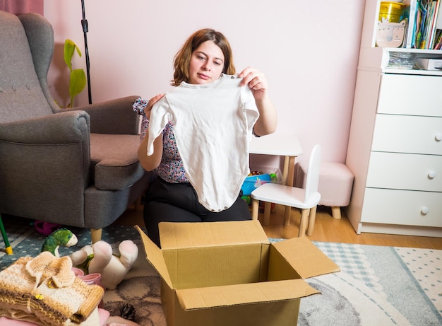 Concetto di donazione di vestiti per bambini invernali. donna che prepara vecchi vestiti usati a casa.