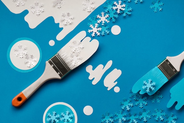 Winter background in blue and white with painting brush loaded with paper snowflakes