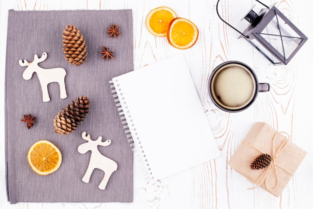 사진 크라프트지 말린 오렌지 커피 컵에 싸인 빈 일기장 나무 사슴 소나무 콘 랜턴 선물이 있는 겨울 배경