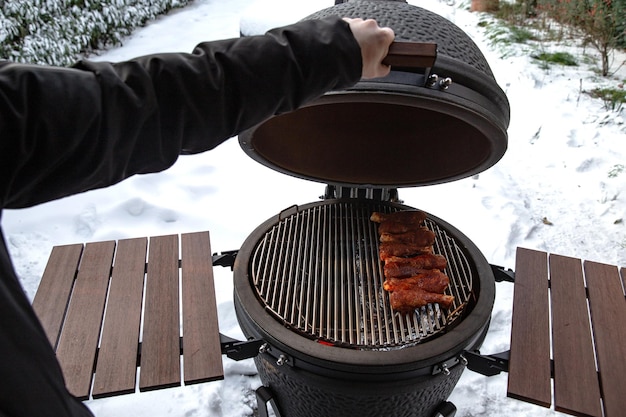 Winter bbq in the fresh white snow Men grilling chicken wings in the winter onn grill