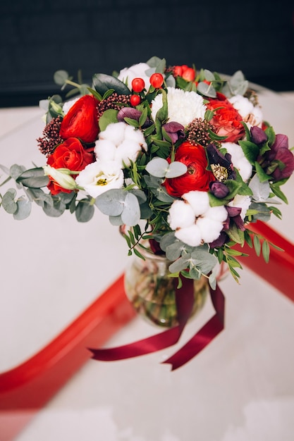 Foto bouquet invernale con rose rosse, cotone, eucalipto. bouquet con nastro rosso. ranuncolo rosso